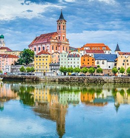 A serene riverscape with colorful historic buildings and a church reflecting in the water under a partly cloudy sky, evoking a peaceful, picturesque ambiance.
