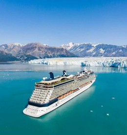 A cruise ship sails in turquoise waters near snow-capped mountains and glaciers, under a clear blue sky, creating a serene and majestic scene.